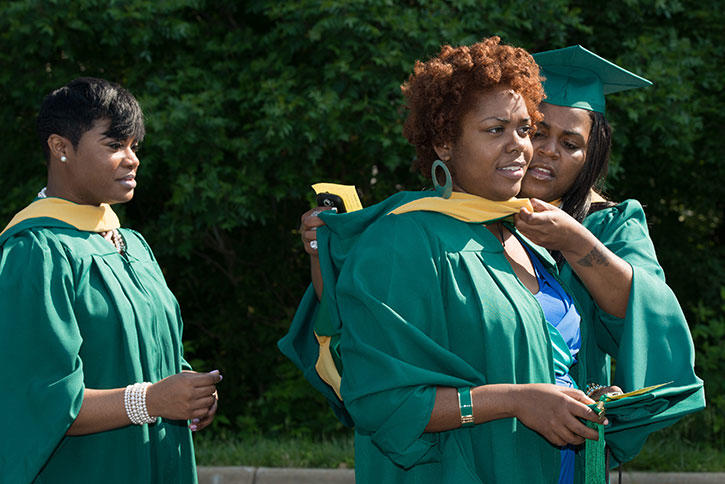 Student helping another student with gown before graduation.