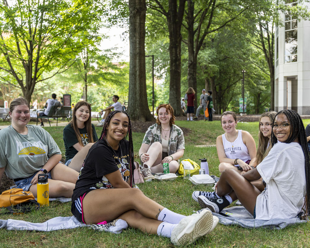 New Mason students sit in a circle outside on the grass.
