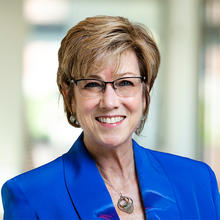 Smiling woman with short hair wearing glasses and a royal blue blazer.