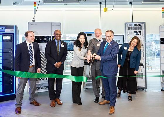 Group of people icut green ribbon in front of large lab equipment.
